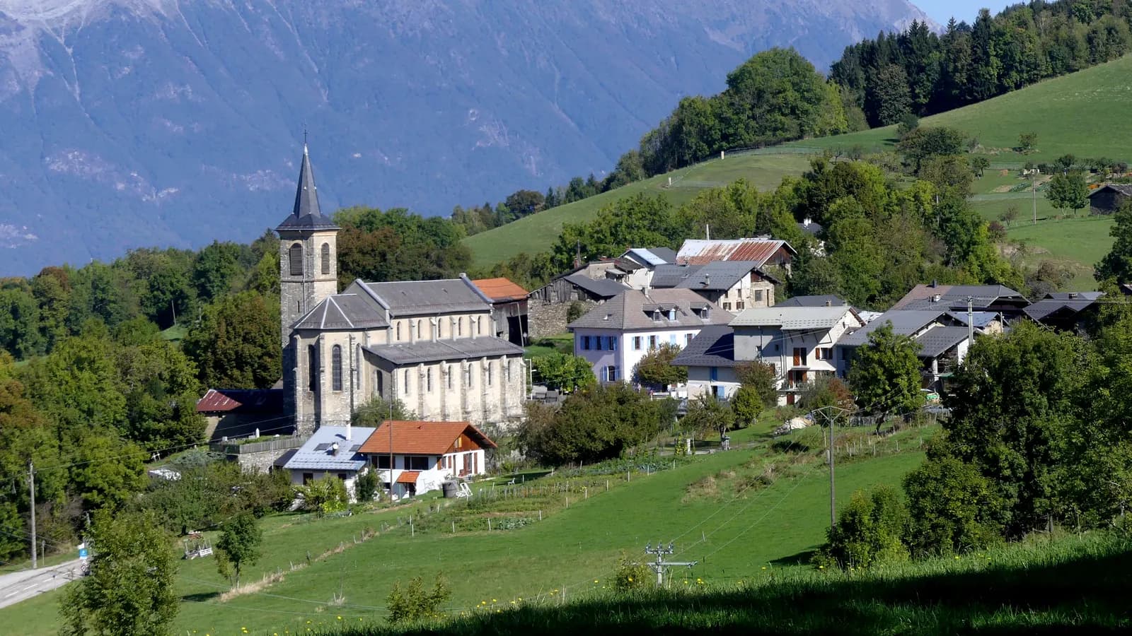Village de montagne avec son église et ses maisons entourées de prairies, au pied des sommets en Savoie