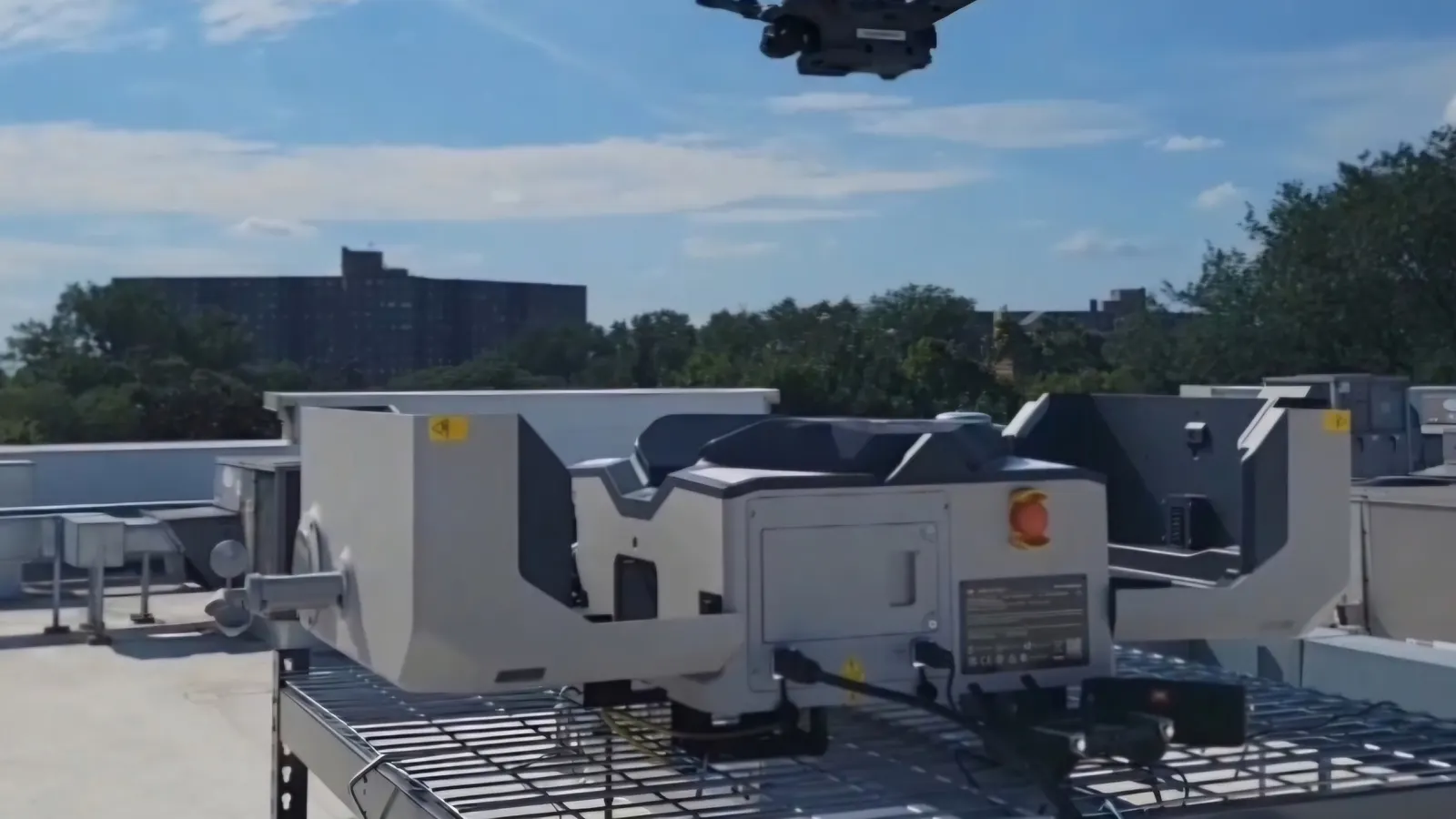 Drone en vol au-dessus de sa station d'accueil automatisée installée sur un toit, sous un ciel bleu