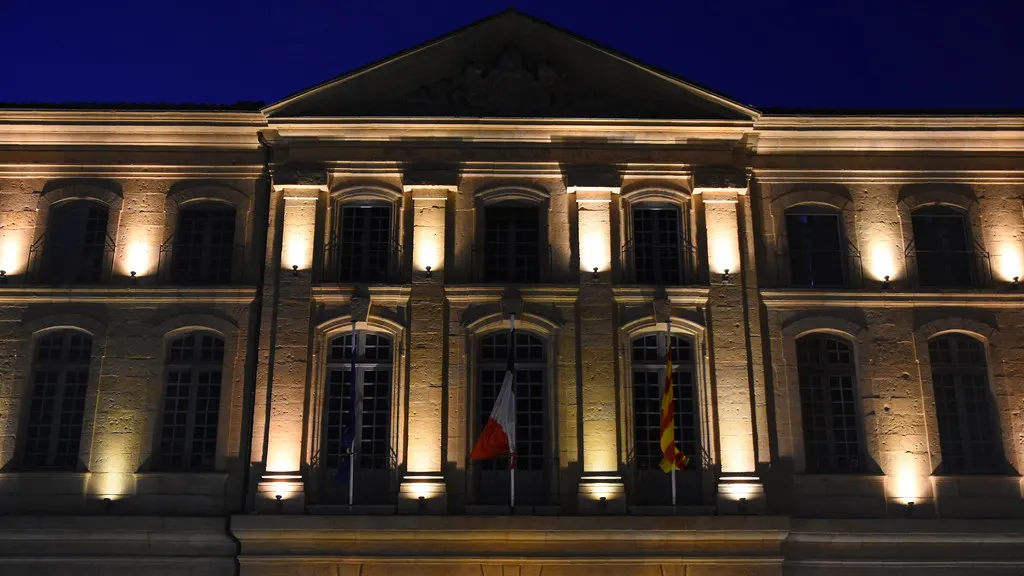 Façade d'une mairie éclairée de nuit, fenêtres allumées dans une rue calme