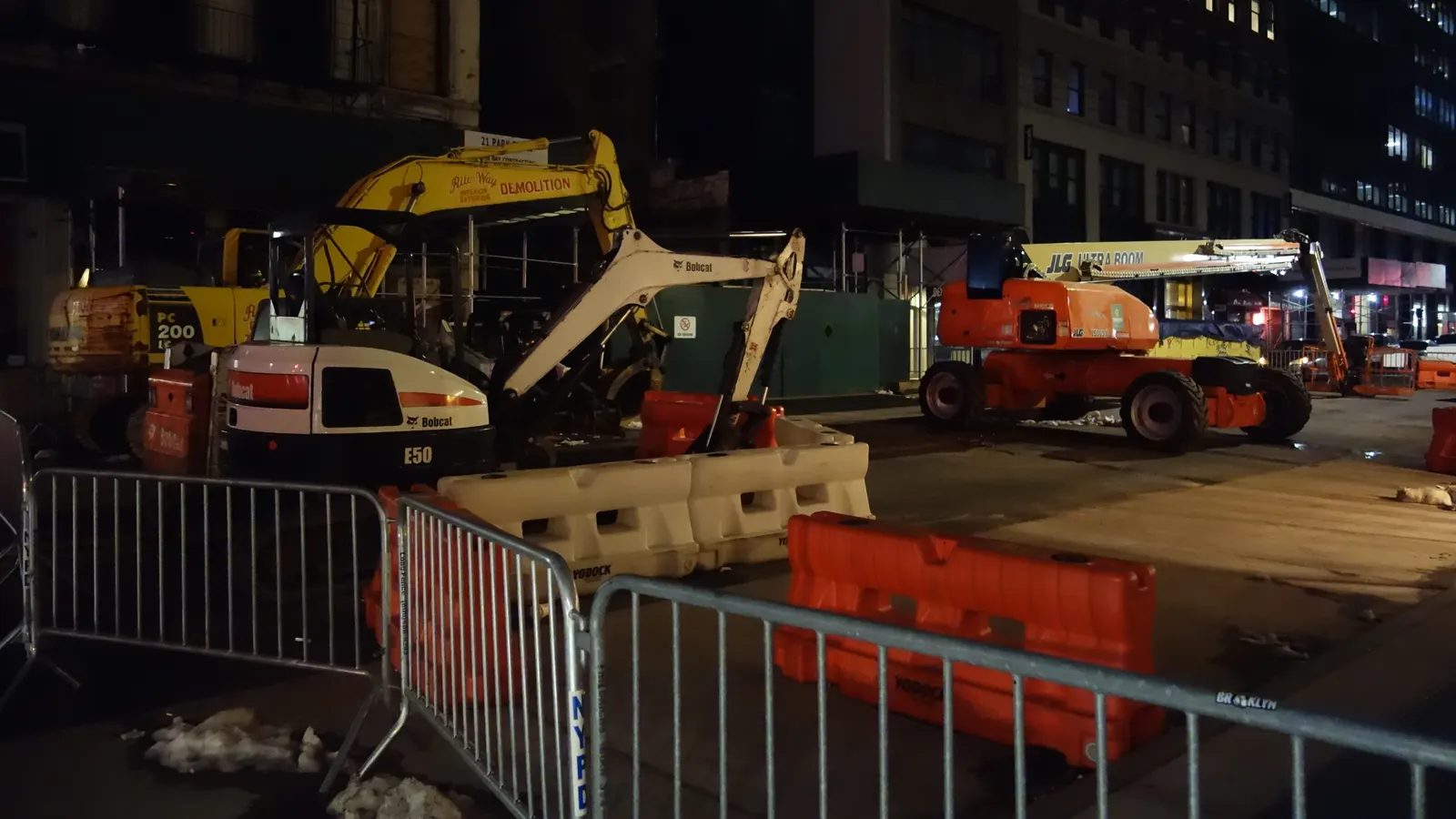 Engins de chantier stationnés de nuit derrière des barrières métalliques sur un chantier urbain éclairé